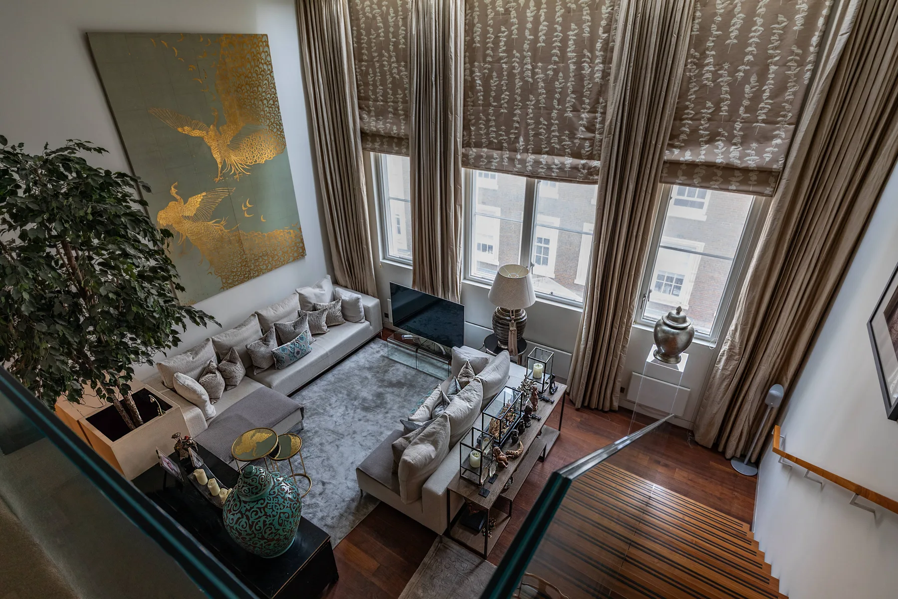 A living room with seating arranged around a coffee table beneath tall windows.