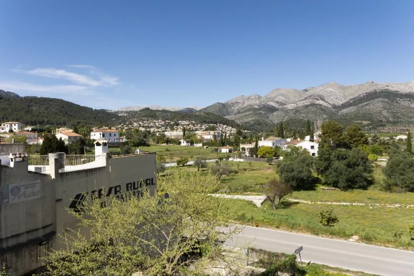 Un paisaje rural con edificios dispersos, campos verdes y montañas a lo lejos.