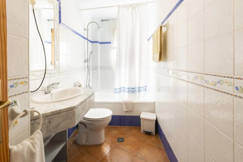 Un baño alicatado con lavabo, inodoro y ducha con cortina.