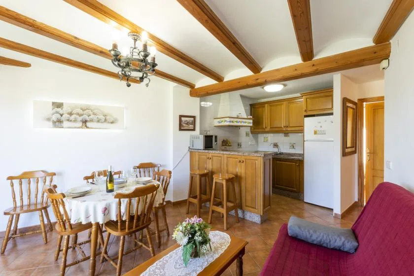 Zona de comedor y cocina con una mesa de madera y asientos junto a la barra.