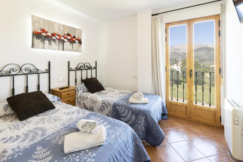 Un dormitorio con camas gemelas, ropa de cama estampada y puertas de vidrio hacia un balcón.