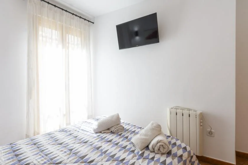 Un dormitorio con una cama estampada, un televisor en la pared y un radiador.