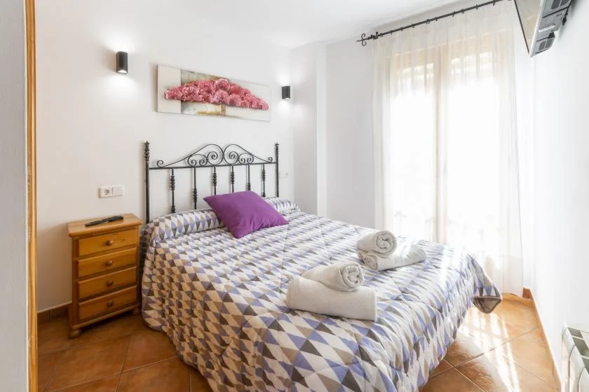 Un dormitorio luminoso con una colcha estampada y cortinas translúcidas.