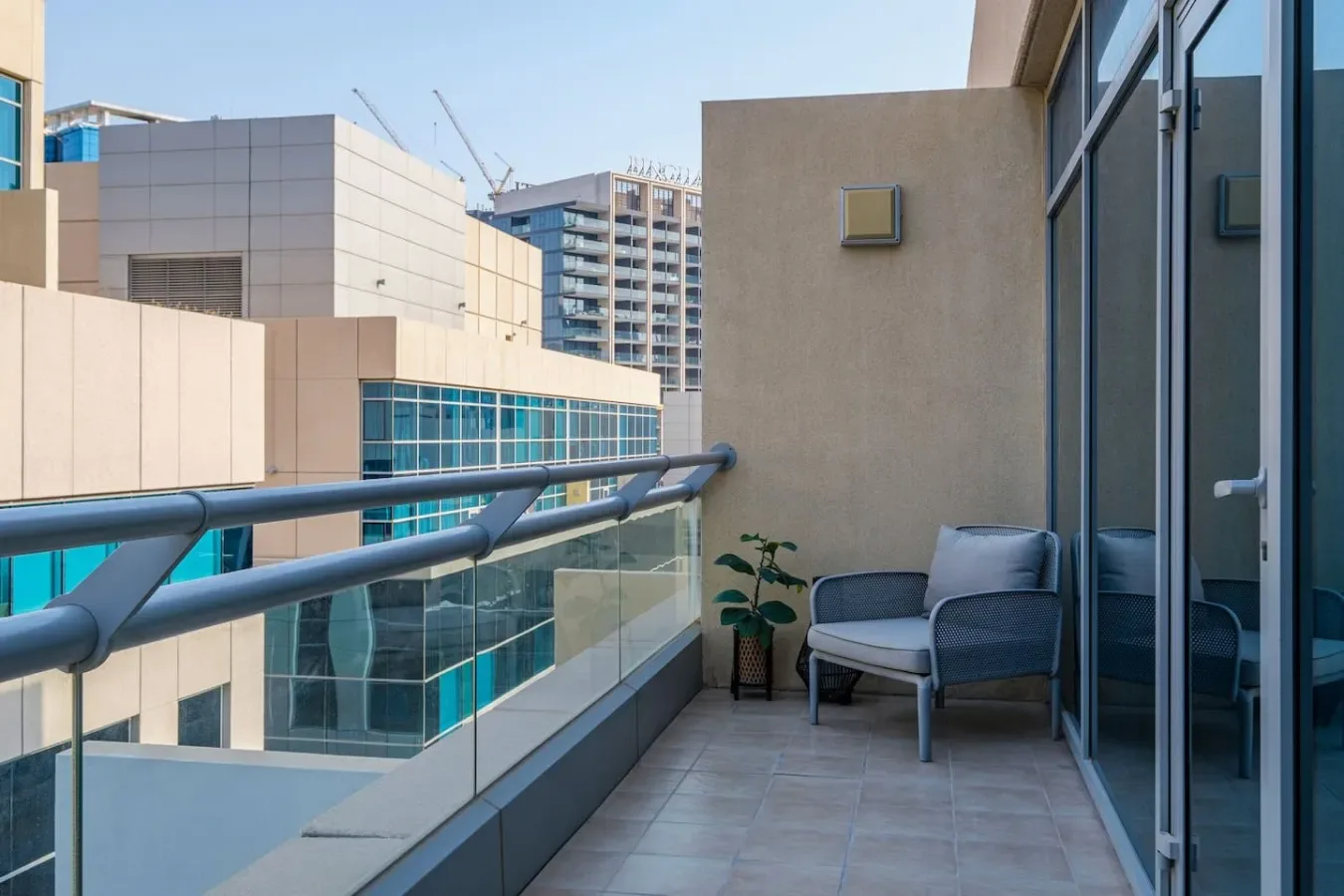 A balcony with seating and glass railings overlooks nearby buildings.