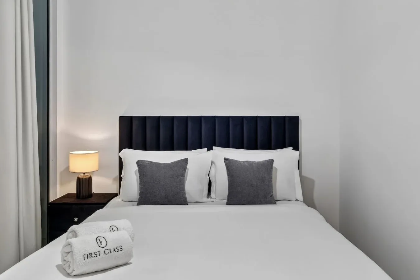A bedroom with a neatly made bed, dark headboard, and bedside lamp.