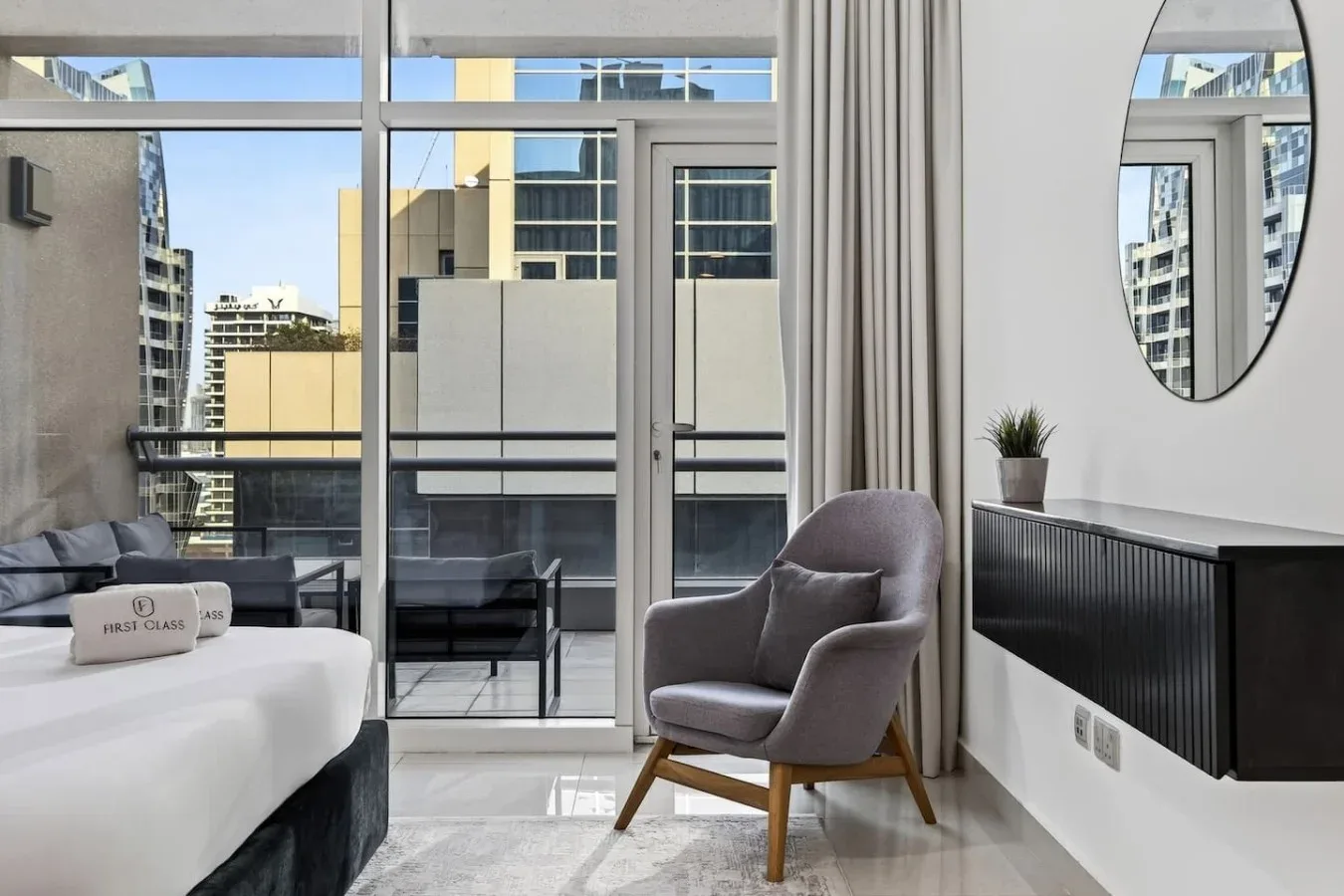 A bedroom with a bed, an armchair, and floor-to-ceiling windows overlooking nearby buildings.