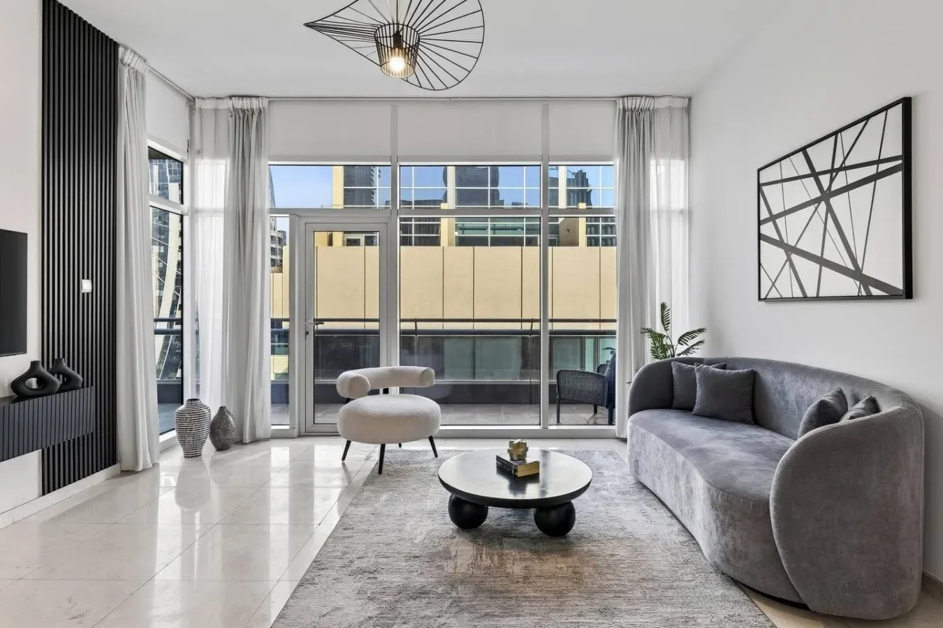 A bright living room with gray seating and large windows overlooking nearby buildings.
