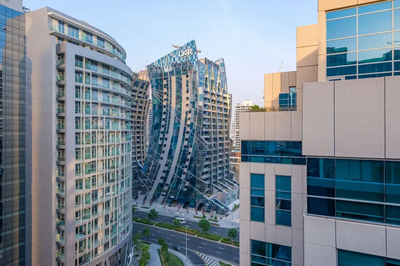 Modern high-rise buildings line a city street beneath a clear sky.