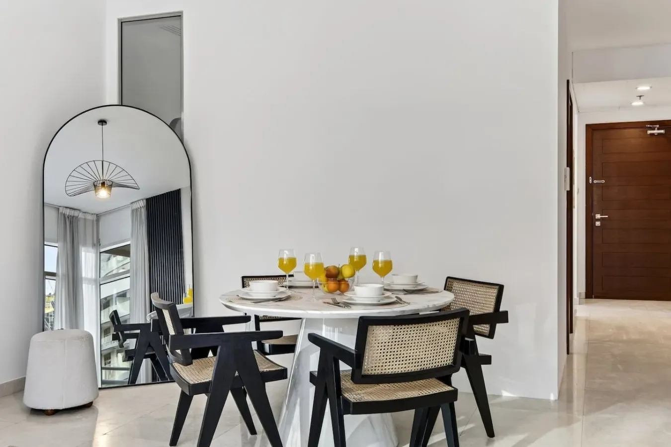 A dining area with a round table and black seating beside a tall mirror.