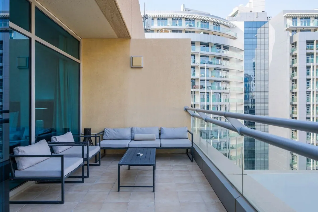 A balcony seating area with a glass railing and views of nearby buildings.