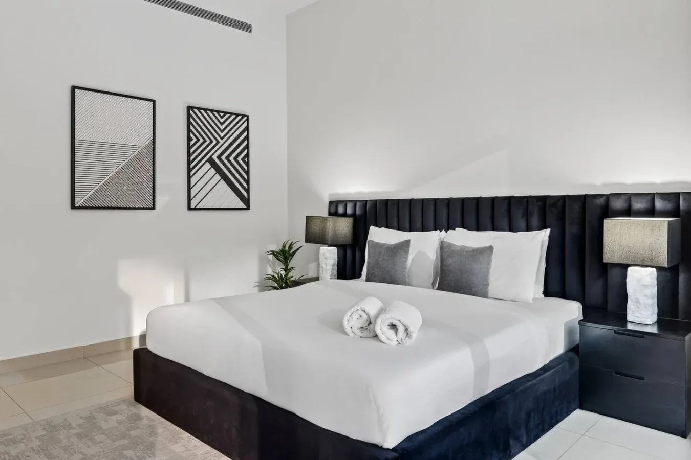 A bedroom with a large bed, dark upholstered headboard, and geometric wall art.