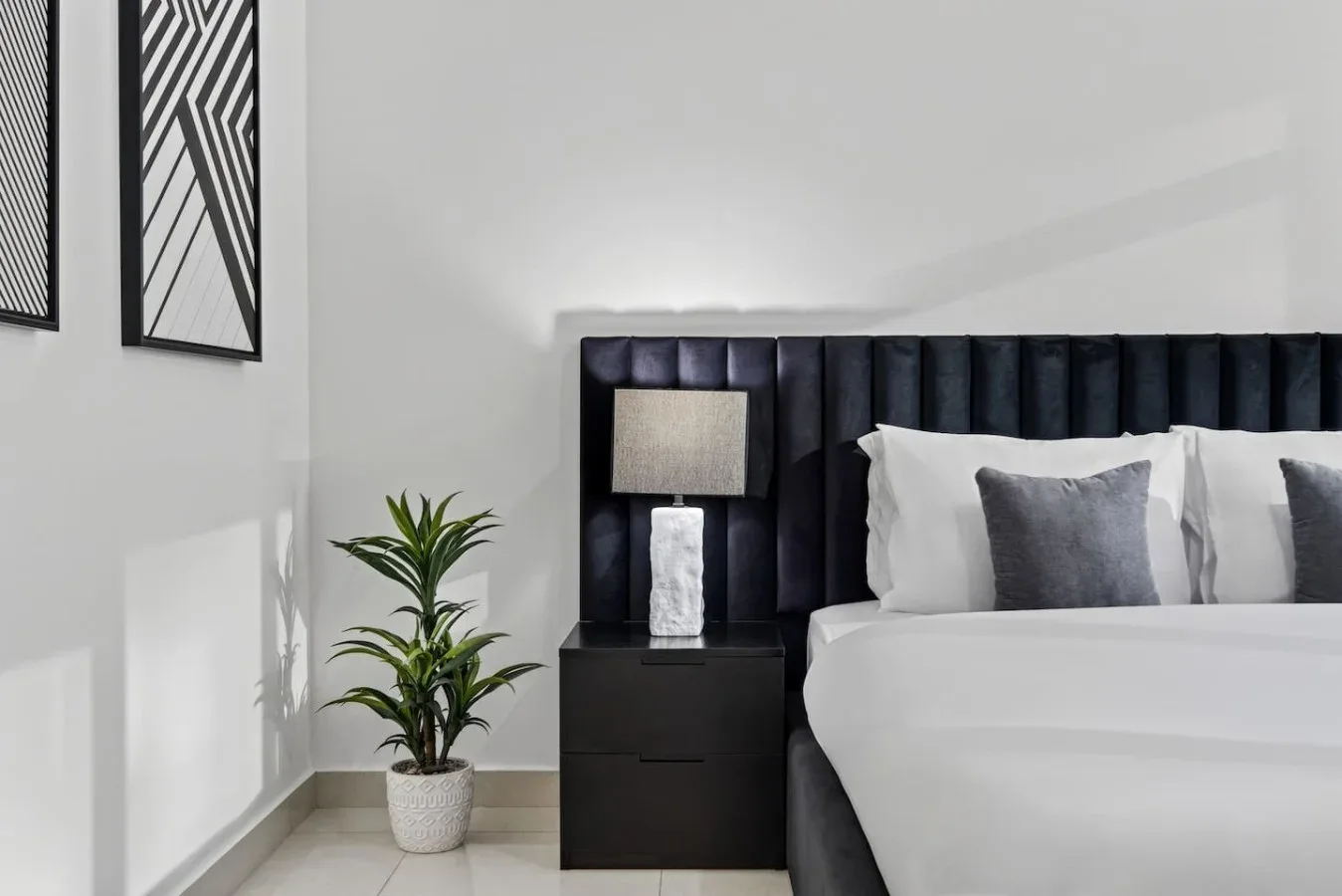 A bedroom with a neatly made bed, dark headboard, and bedside table.