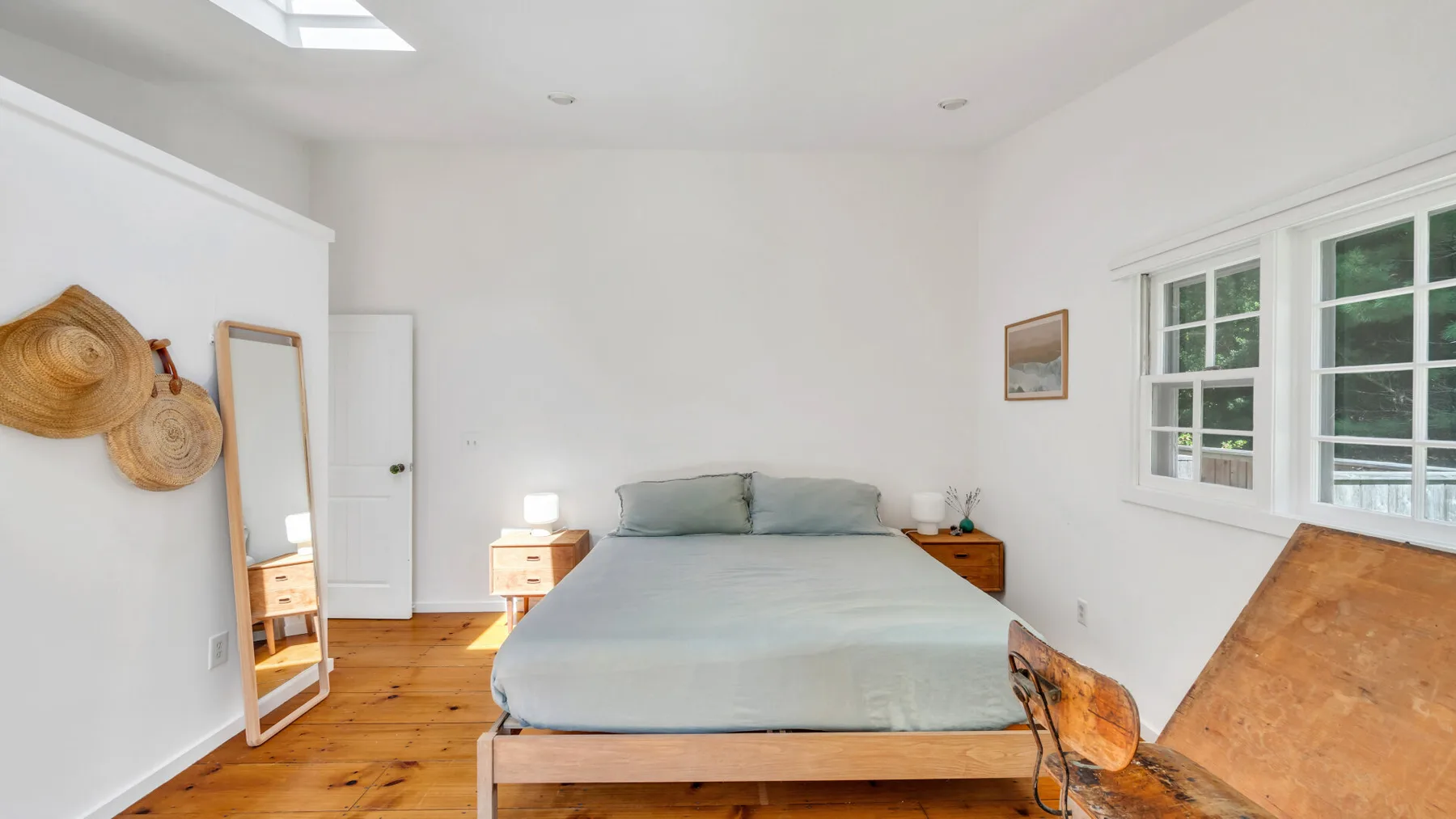 A bright bedroom with a bed, wooden flooring, and windows.