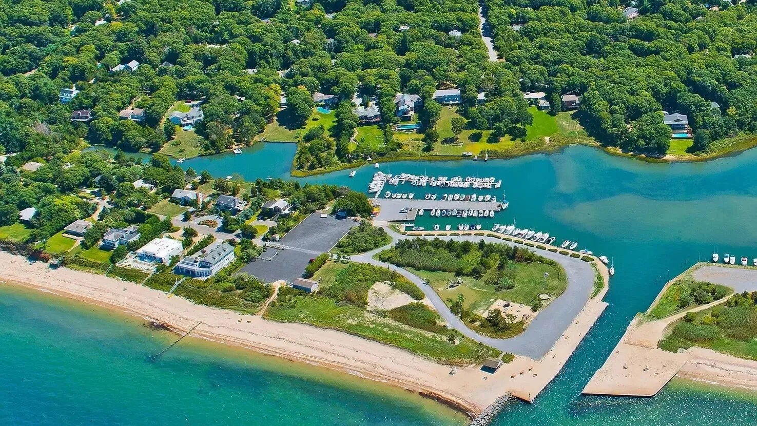 Aerial view of a marina beside a sandy beach and wooded shoreline.