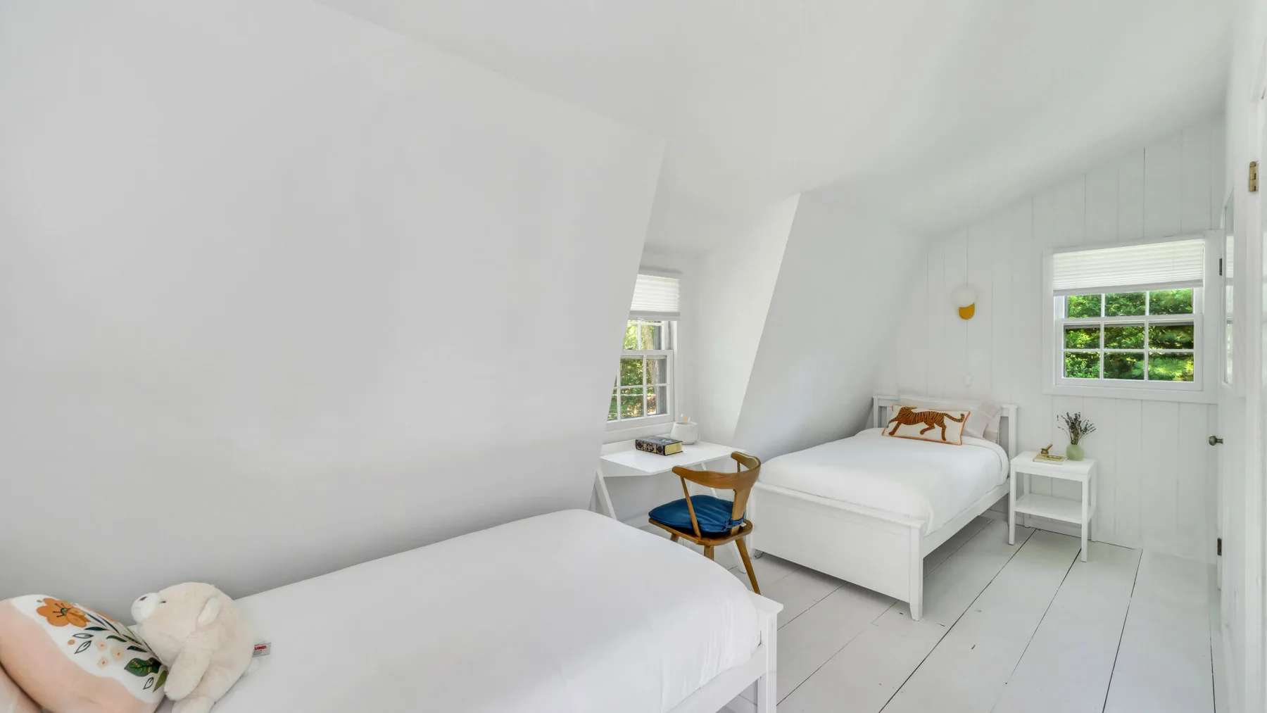 A bright bedroom with two beds and windows along the sloped walls.