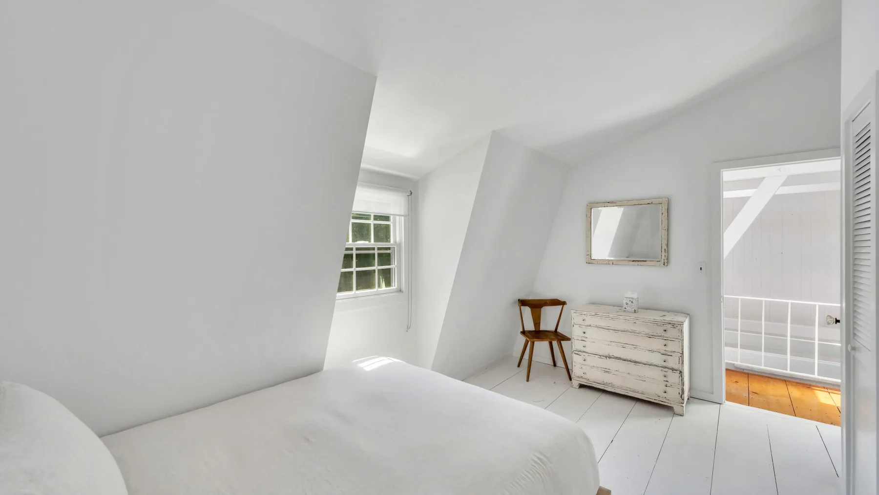 A bright bedroom with a bed, dresser, and an open doorway to a balcony.