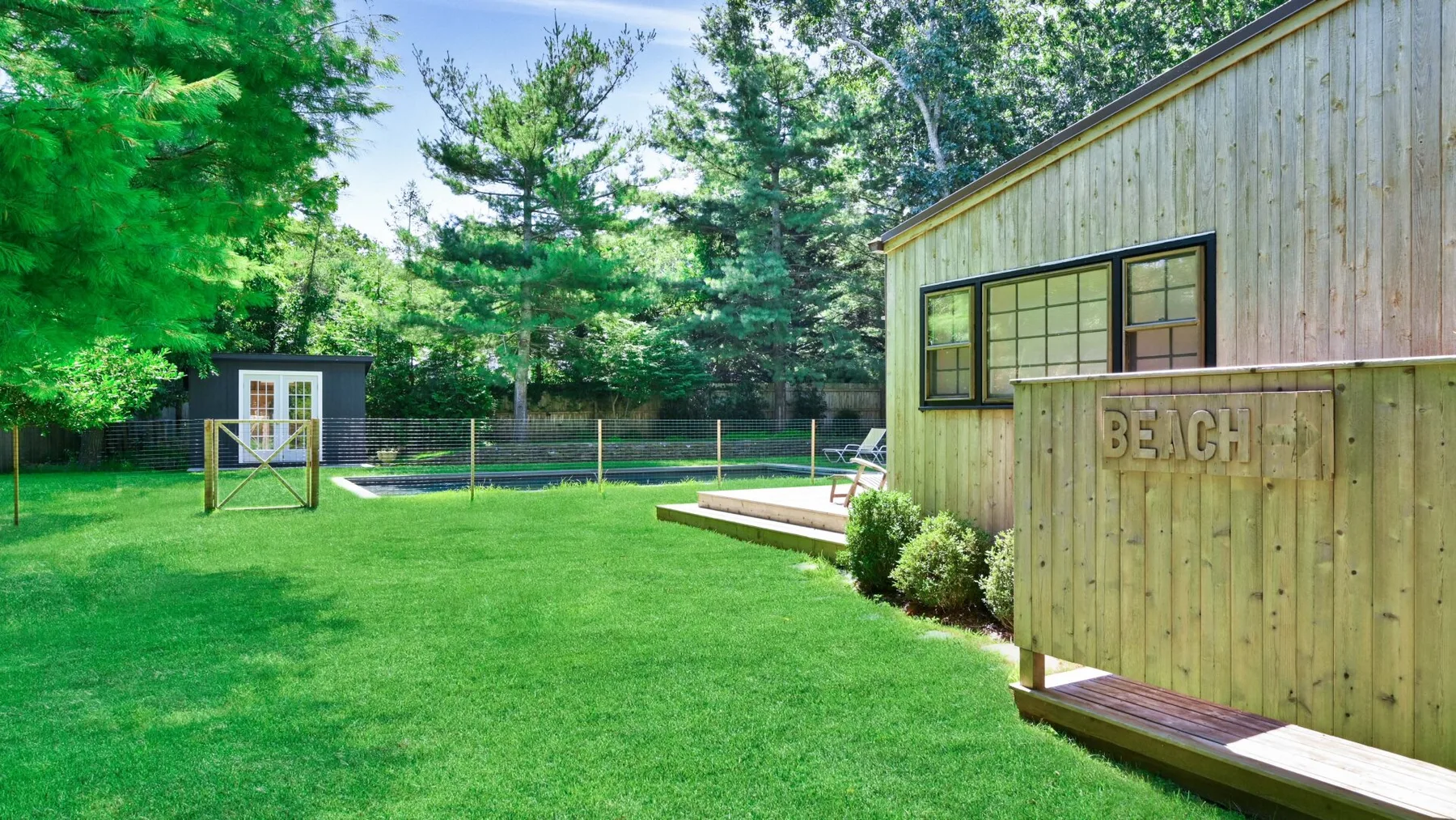A grassy backyard with a wooden building and fenced pool.