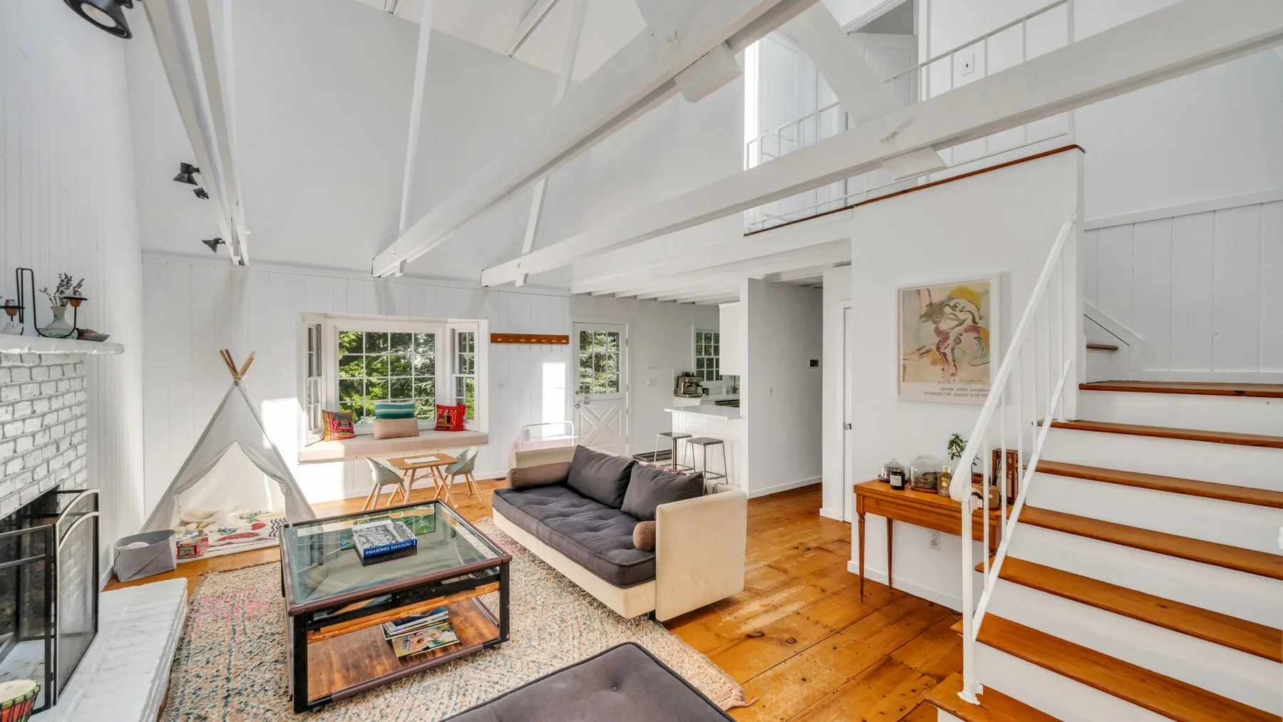 A bright open living room with seating, a coffee table, and stairs to an upper level.