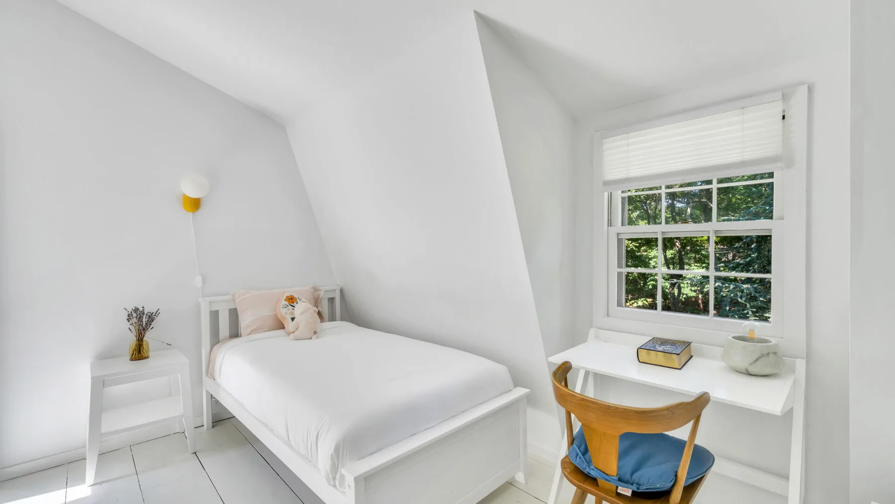 A bright bedroom with a single bed beside a window and small desk.