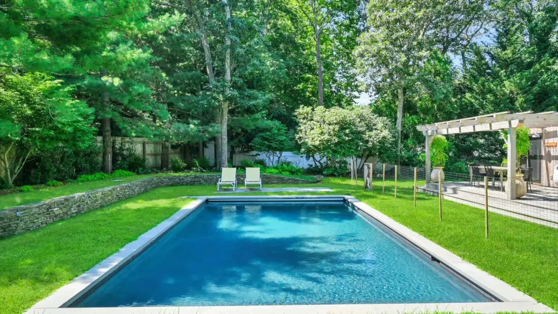 An outdoor swimming pool sits amid a green lawn and mature trees.