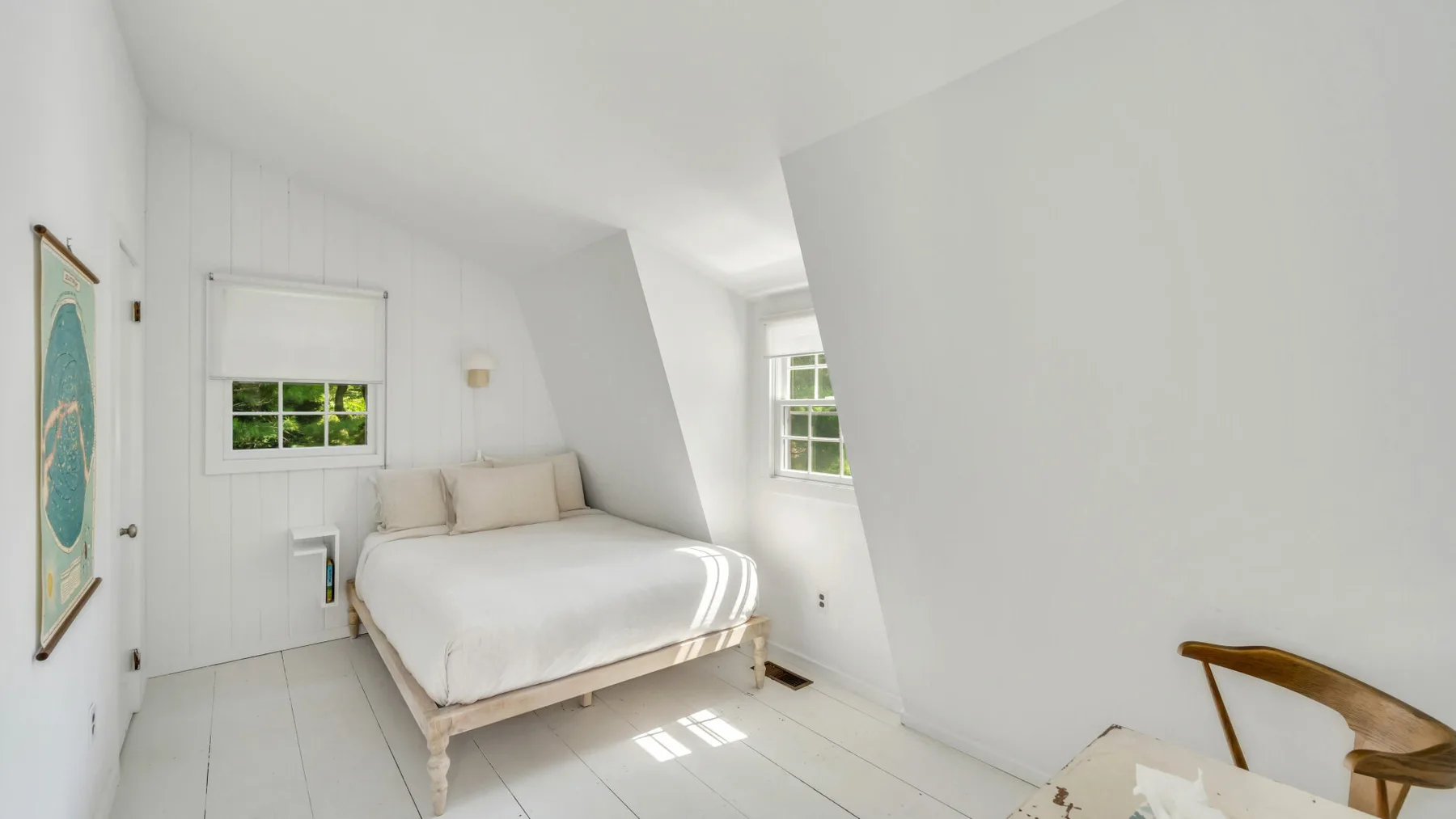 A bright bedroom with a bed beneath sloped walls and windows.