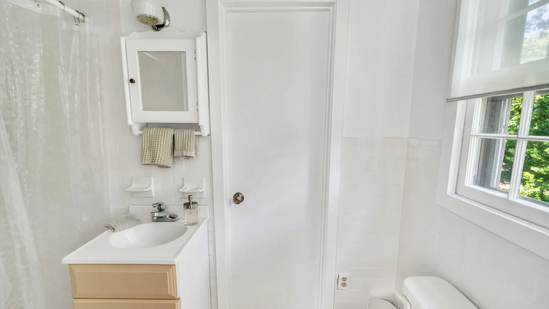 A bright bathroom with a sink, mirror, and window.