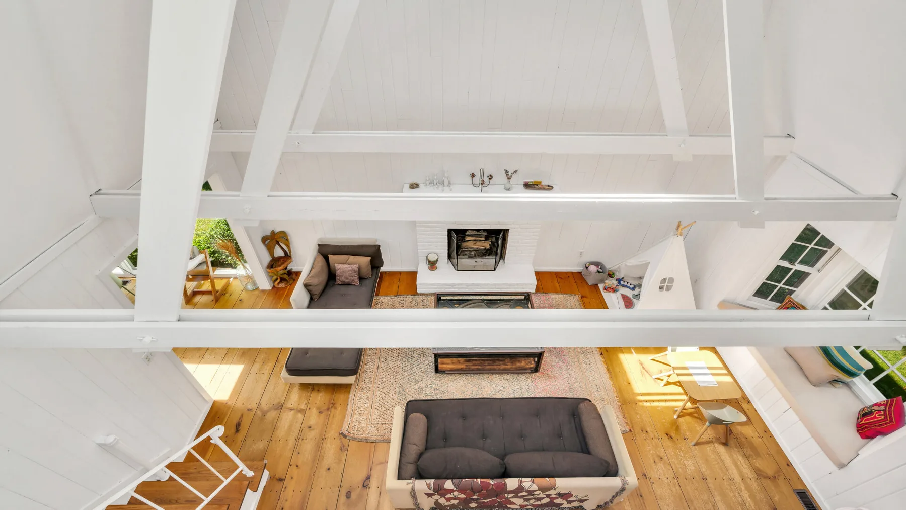 An elevated view of a living room with seating beneath exposed white beams.
