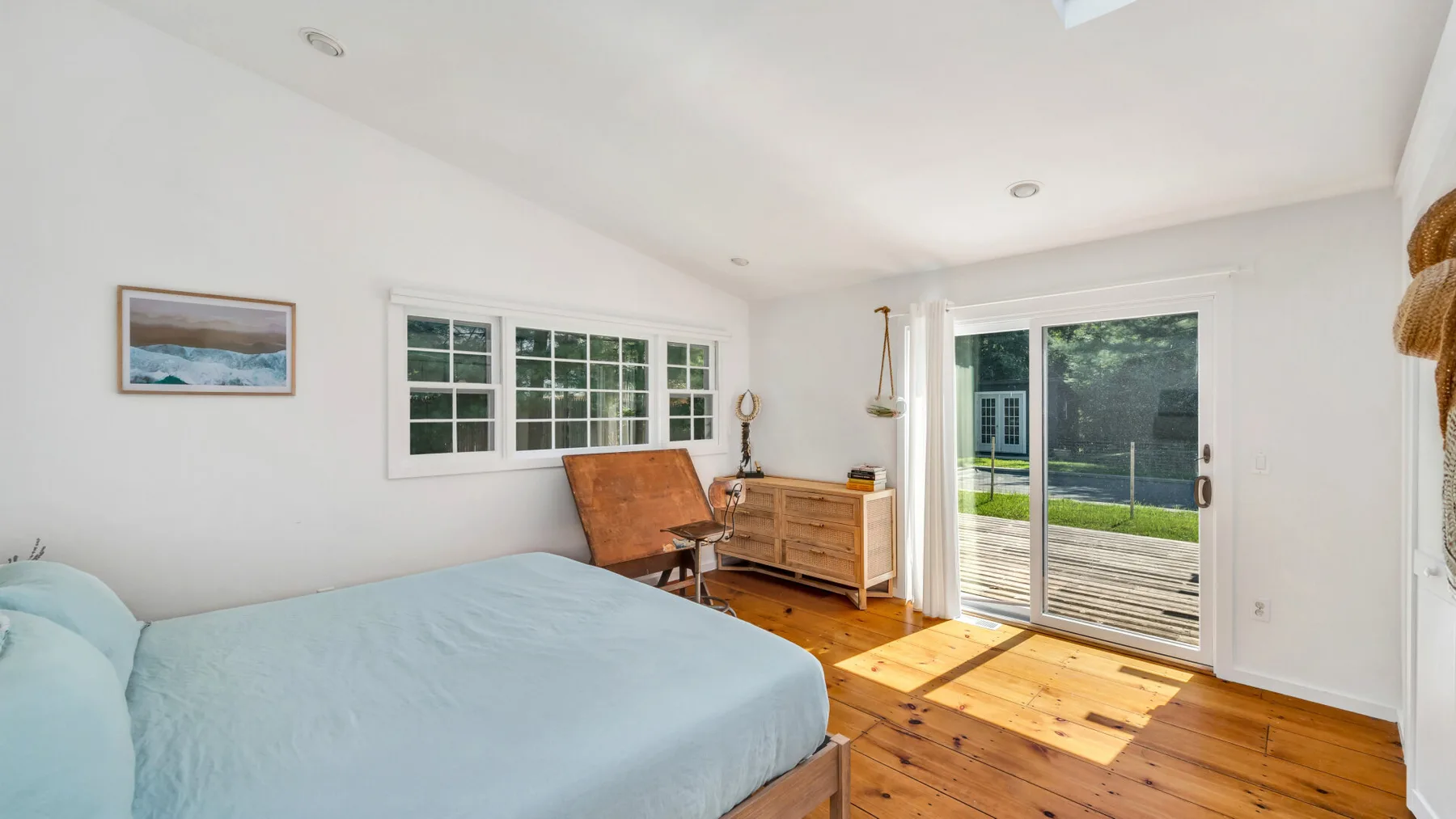 A bright bedroom with a bed beside large windows and a glass patio door.