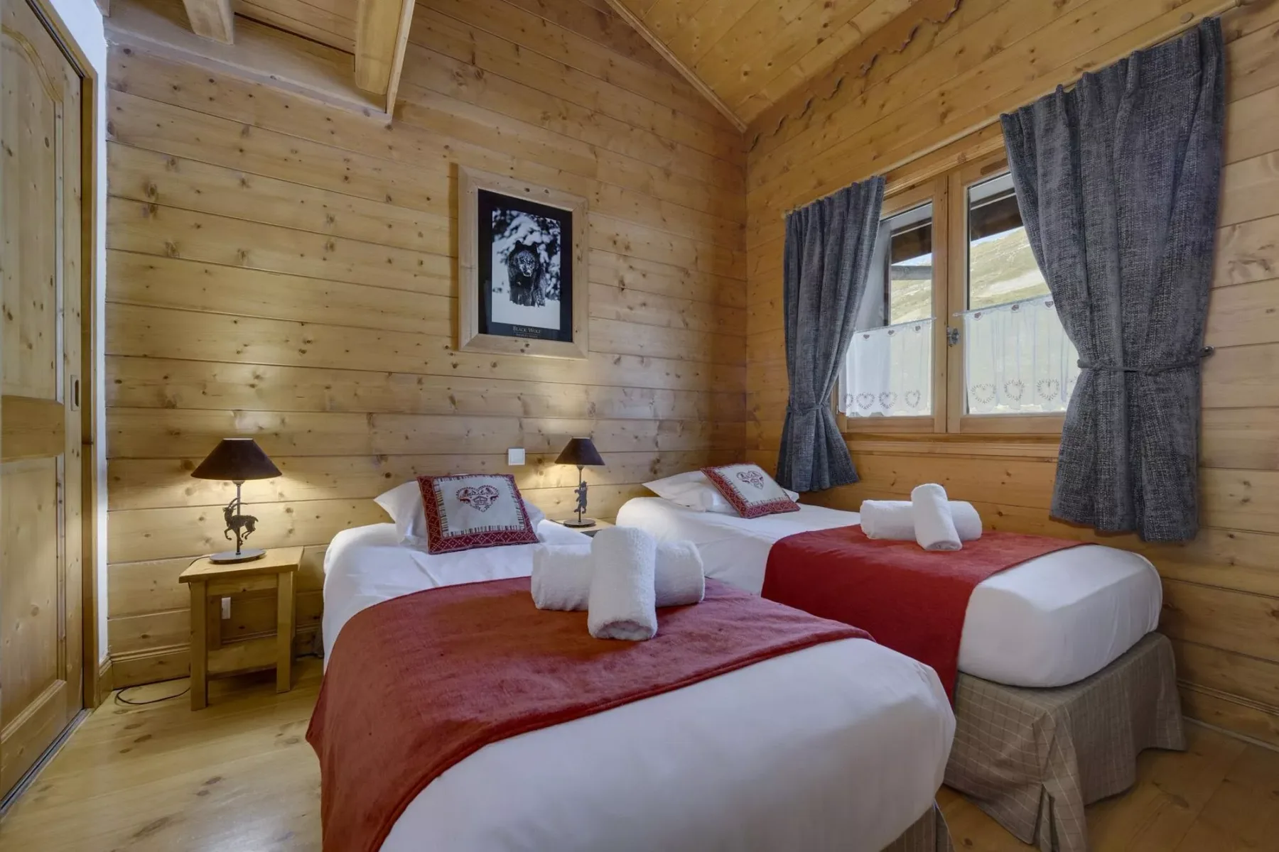 A wood-paneled bedroom with two beds and a window with dark curtains.
