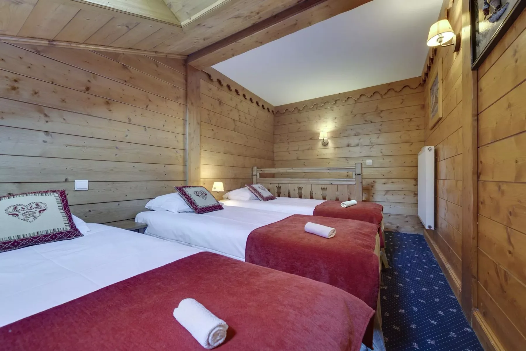 A wood-paneled bedroom with several beds and burgundy bedspreads.