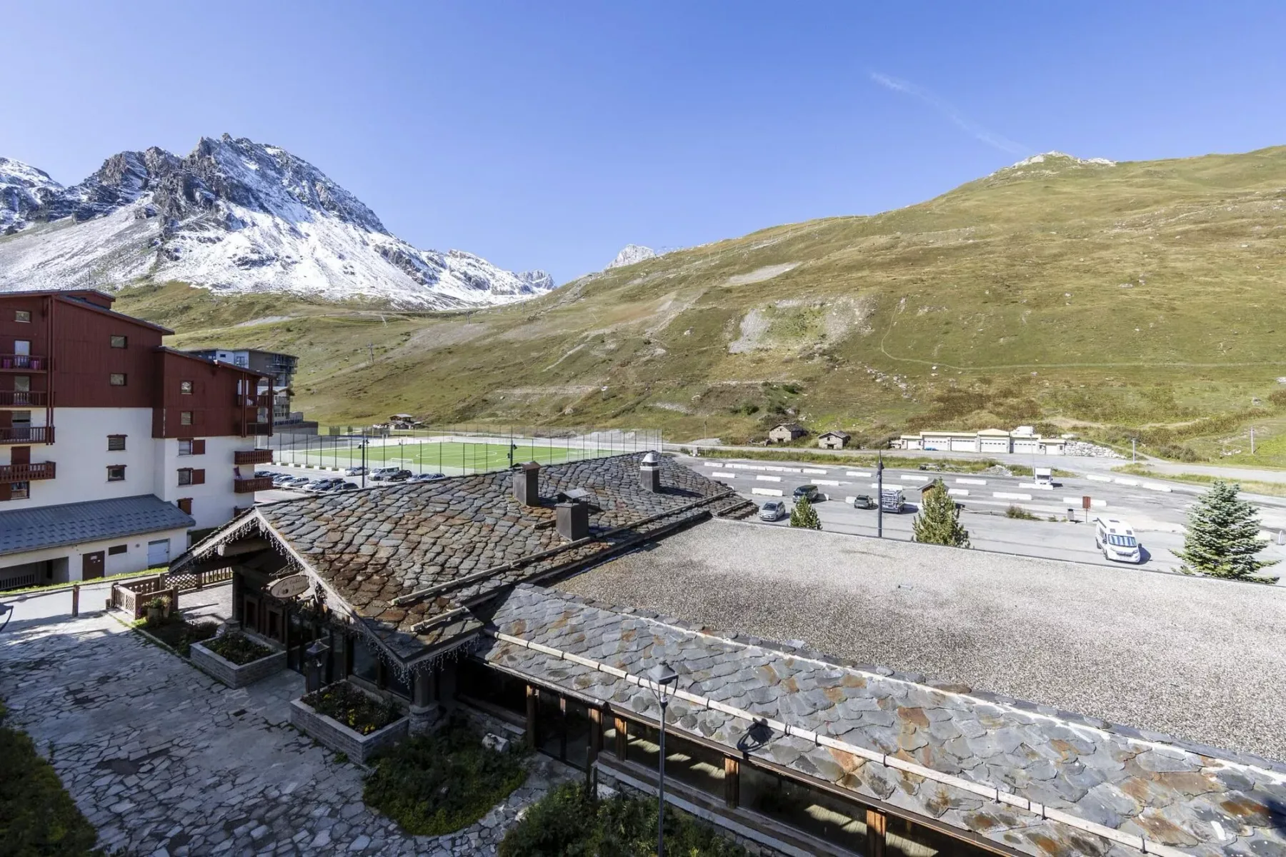 Mountain resort buildings sit below a snow-dusted peak and grassy slopes.