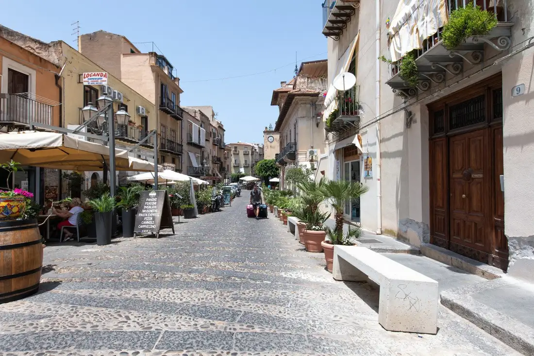 A cobblestone street lined with buildings, outdoor seating, and potted plants.