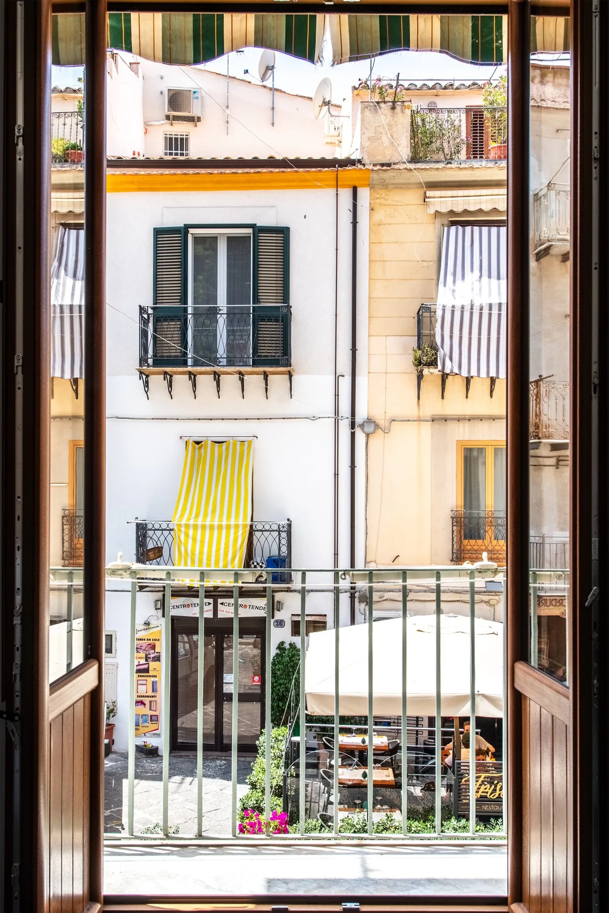 An open window overlooks neighboring buildings and a small street-side café.