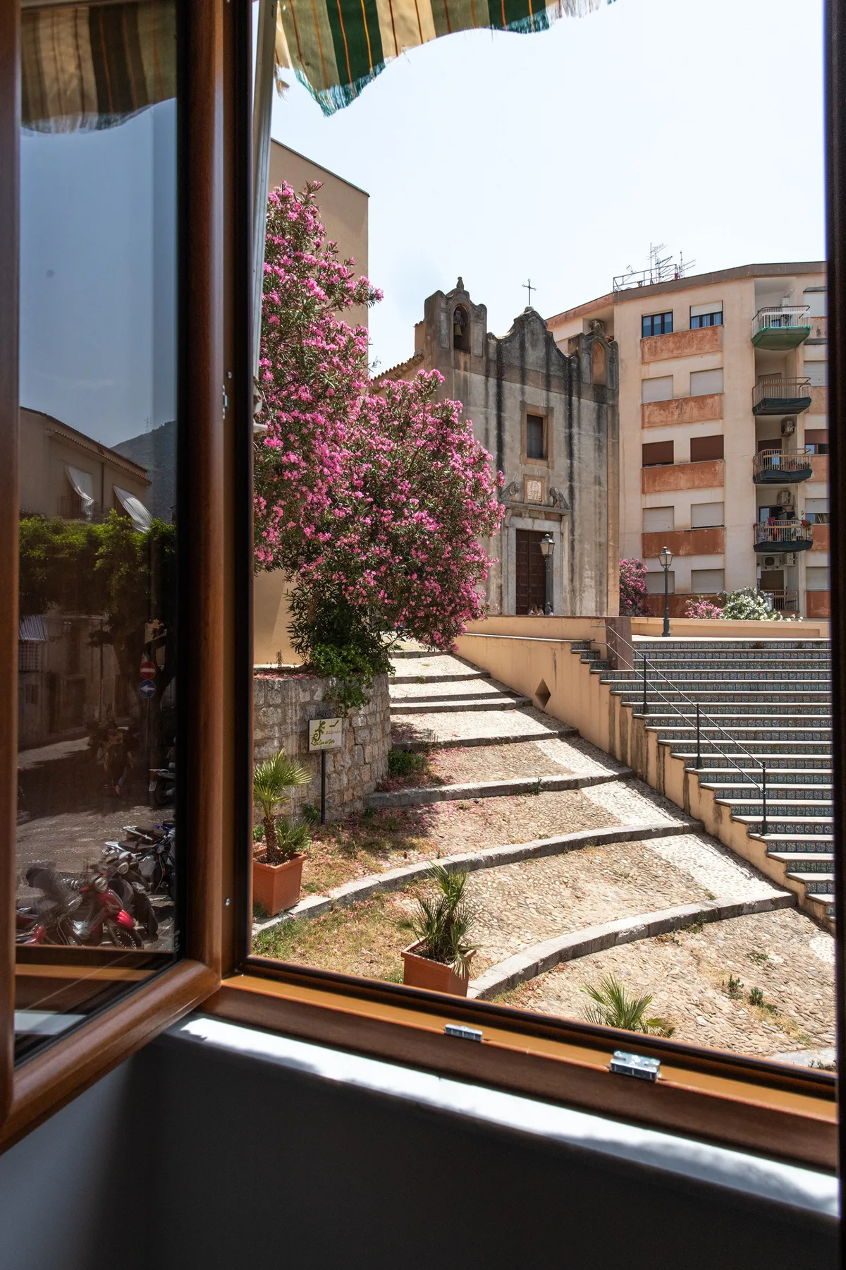 A view through an open window overlooks a flowering tree and stone steps.