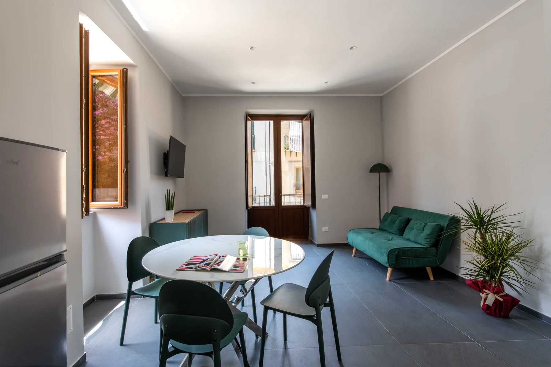 A bright living and dining area with a round table, seating, and a green sofa.