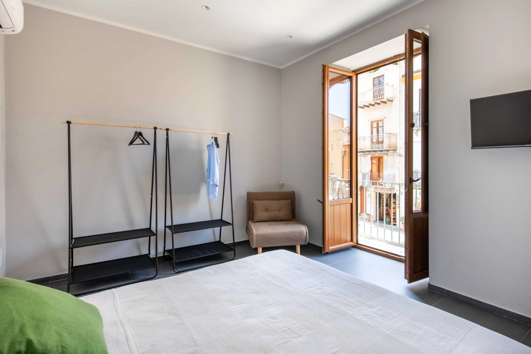 A bright bedroom opens onto a balcony through tall wooden-framed doors.