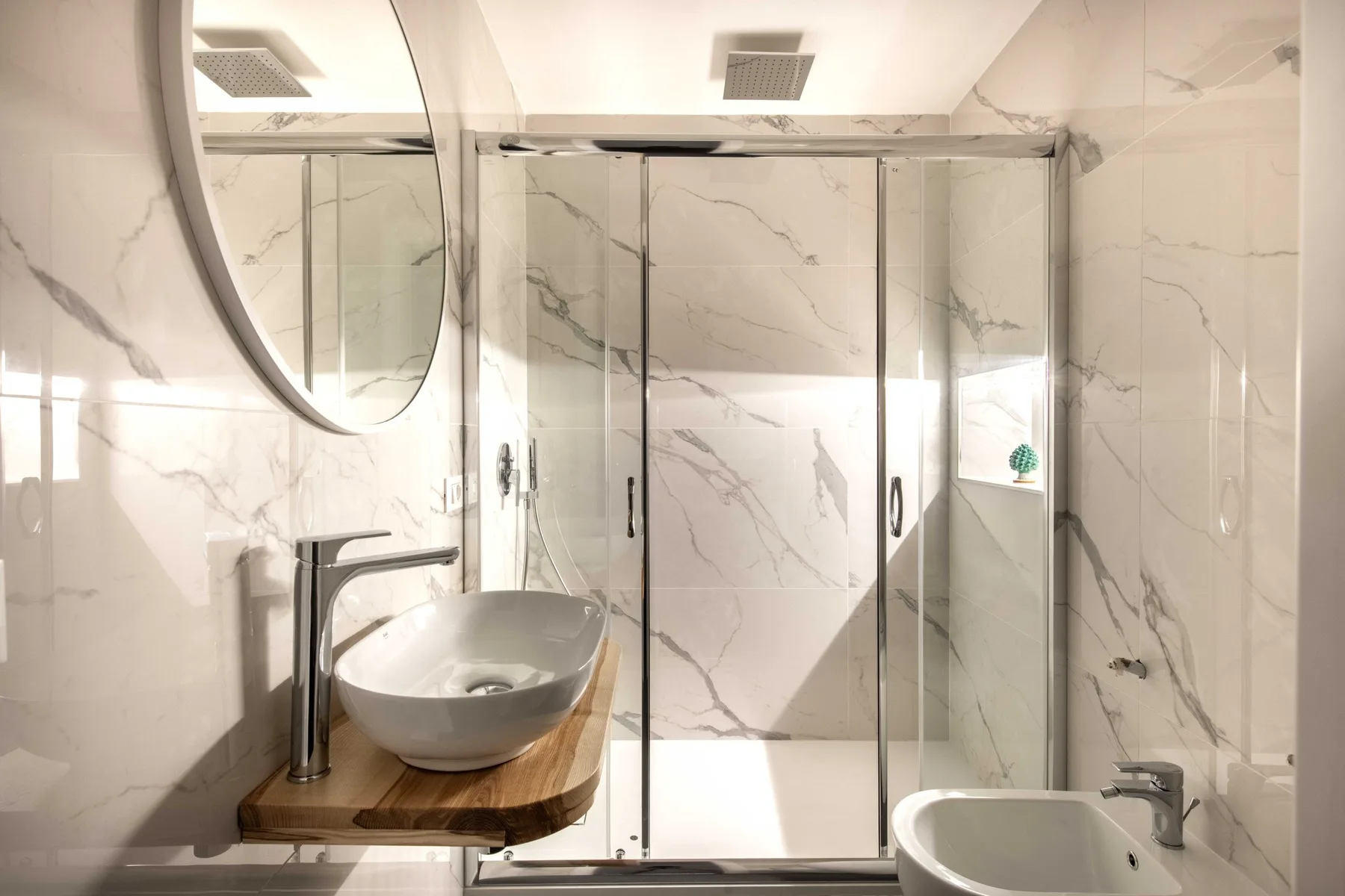 A tiled bathroom with a glass shower, sink, and bidet.