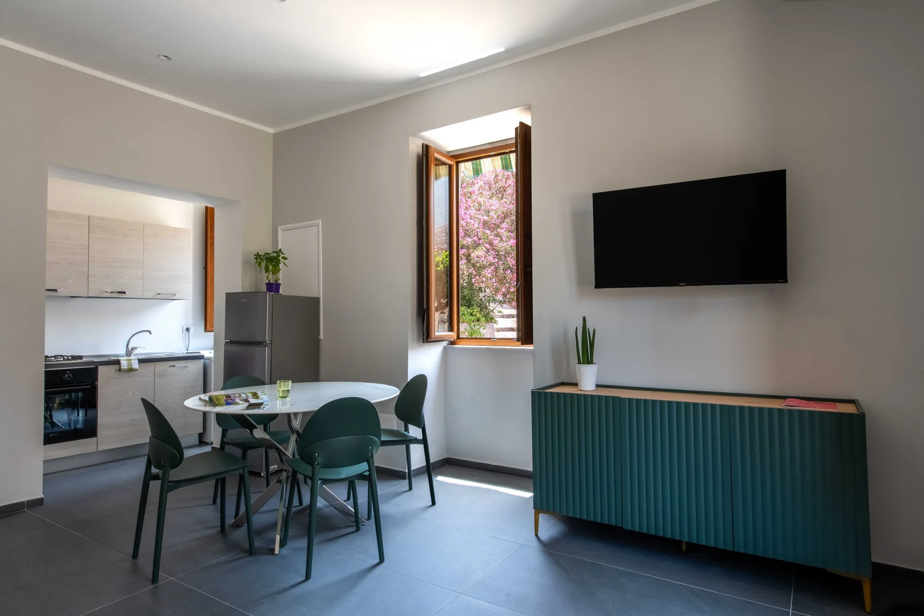 A dining area beside an open kitchen, with a table and wall-mounted television.
