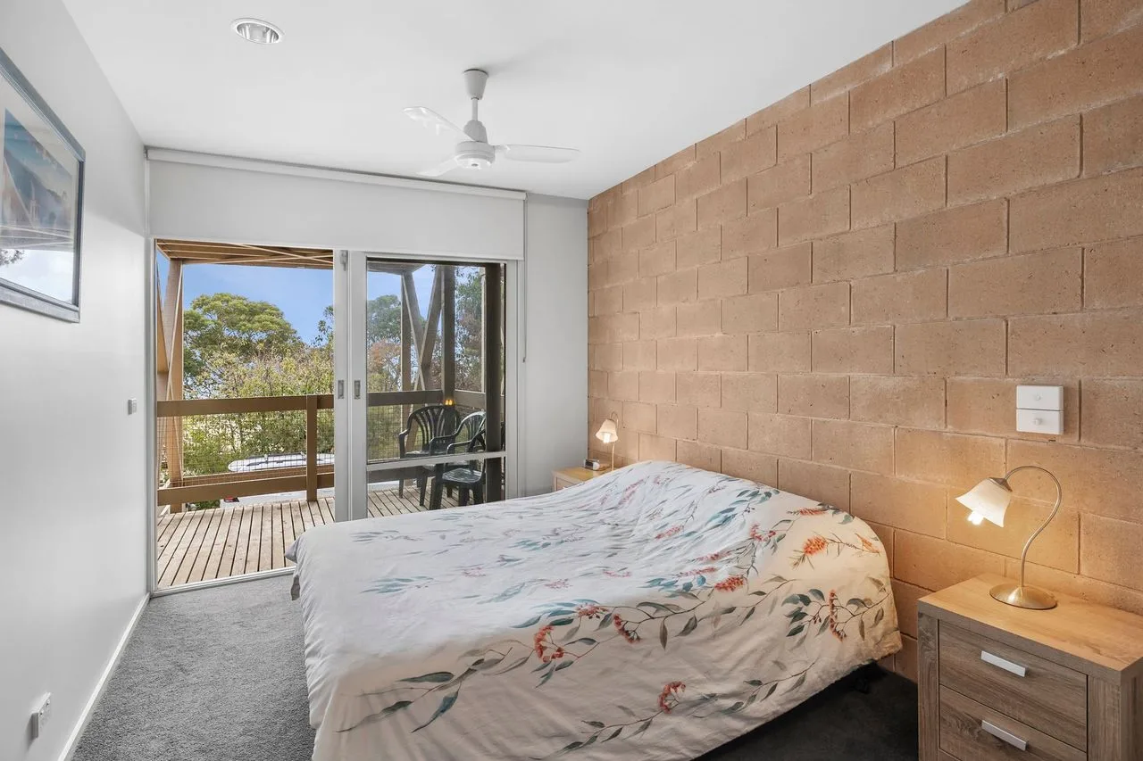 A bedroom with a bed beside sliding glass doors opening onto a balcony.