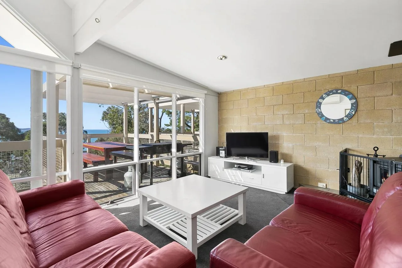 A living room with red seating, a coffee table, and wide windows.
