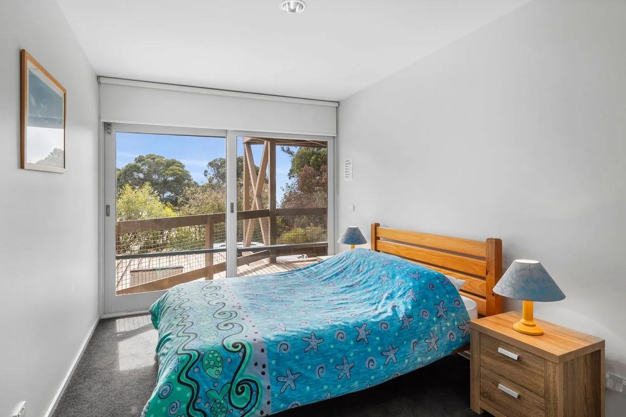 A bedroom with a bed beside sliding glass doors opening onto a leafy view.