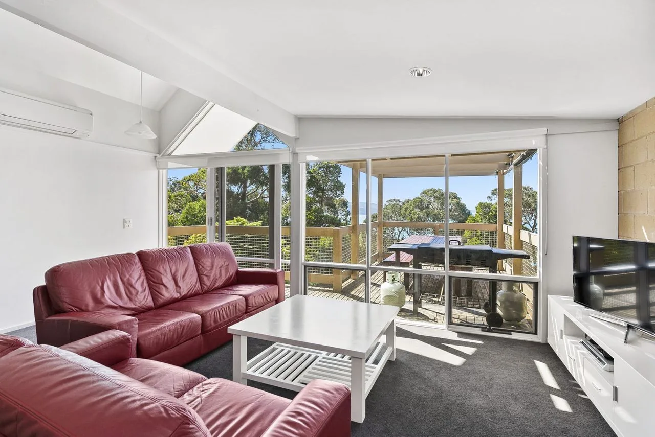 A bright living room opens onto a deck, with red seating and a coffee table.