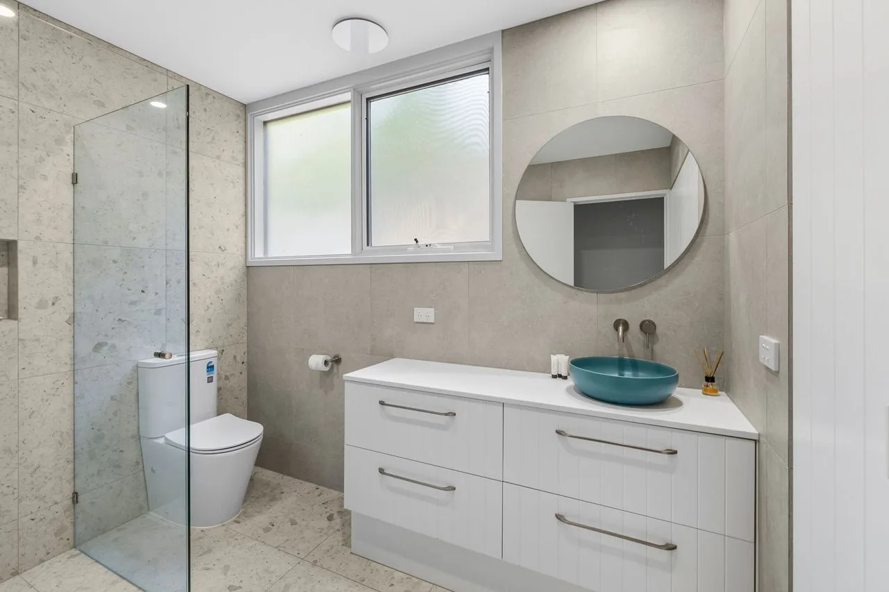 A bright bathroom with a glass shower, toilet, and vanity.