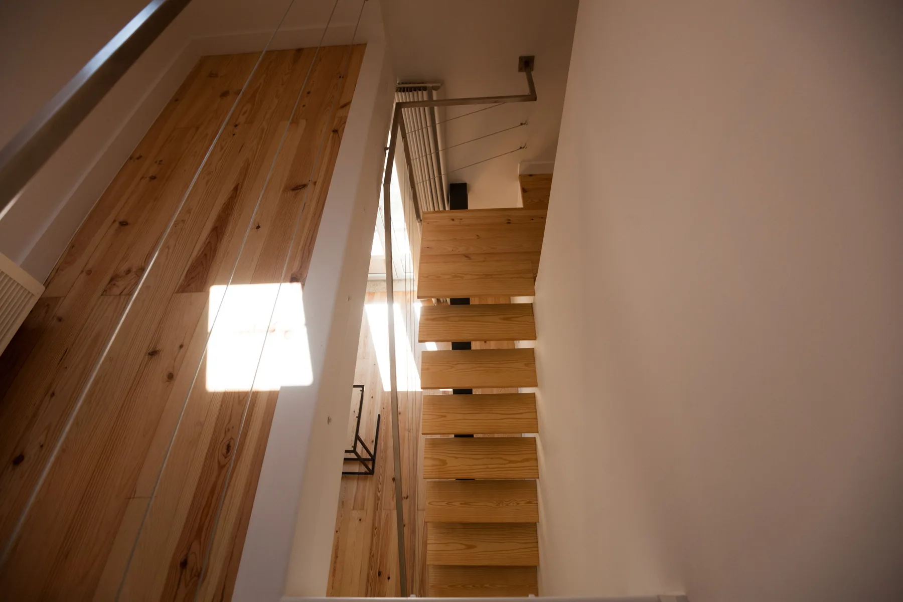 Una escalera de madera sube junto a una pared alta revestida de paneles.