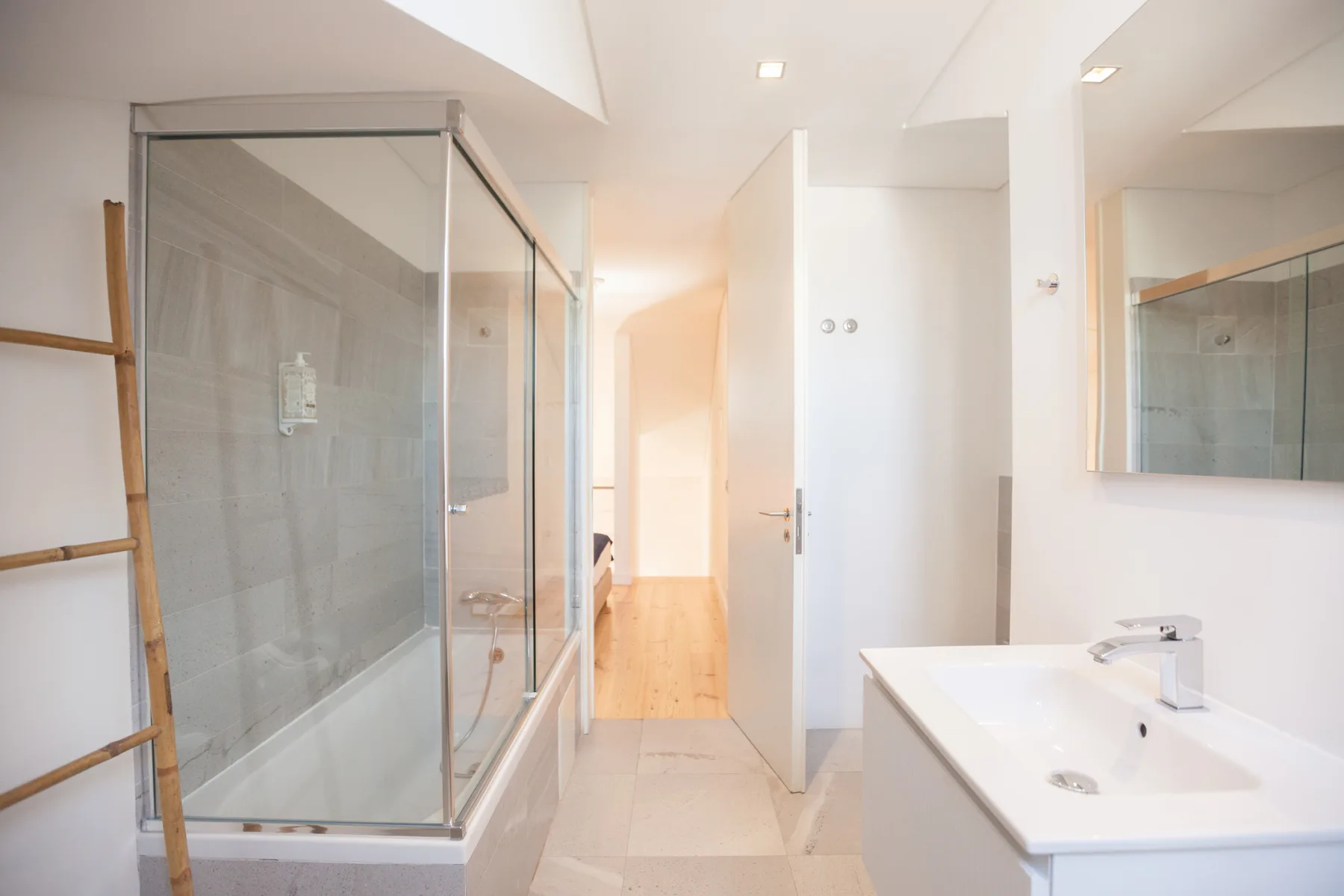 Un baño luminoso con una ducha de vidrio y un lavabo blanco.