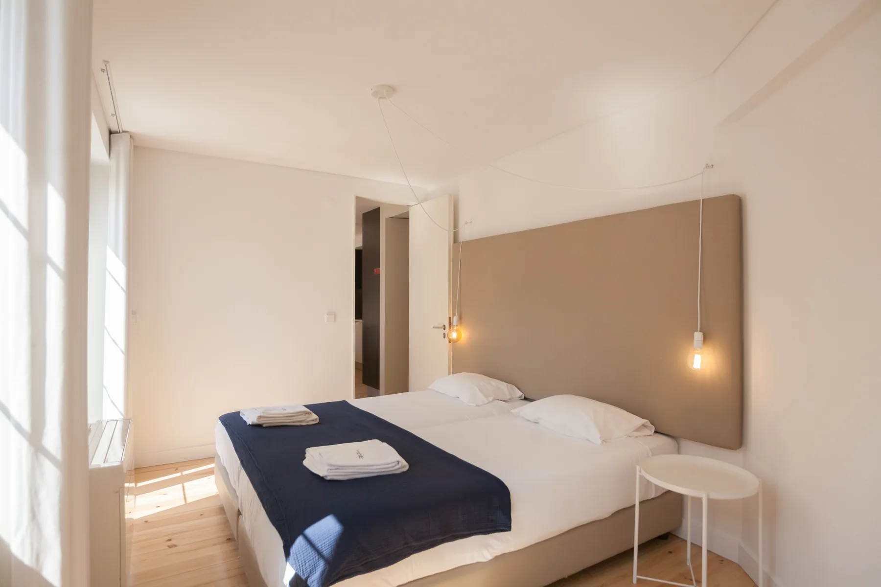 Un dormitorio luminoso con una cama doble y una mesa auxiliar.