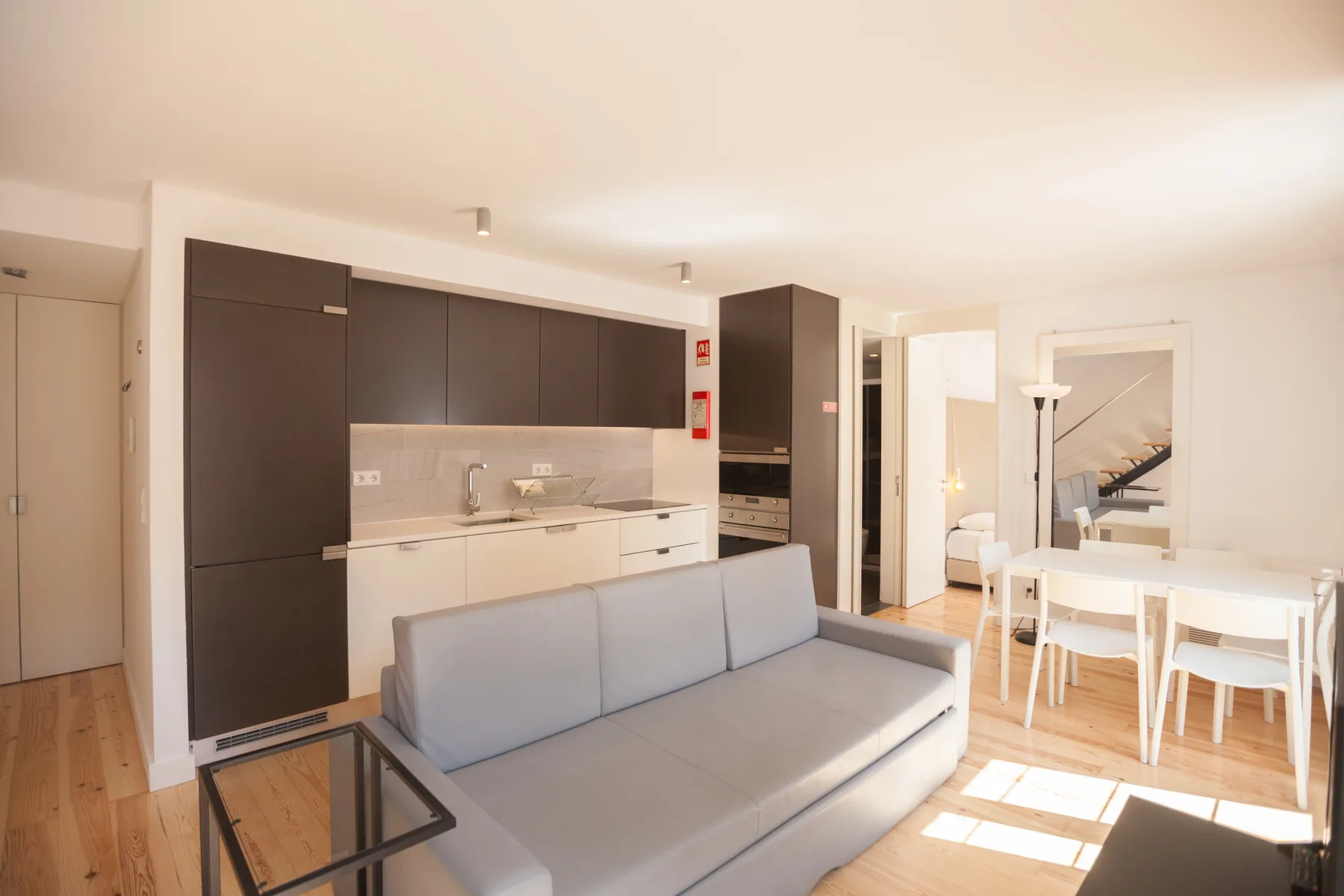 Una luminosa sala de estar y comedor con sofá, mesa y cocina abierta.