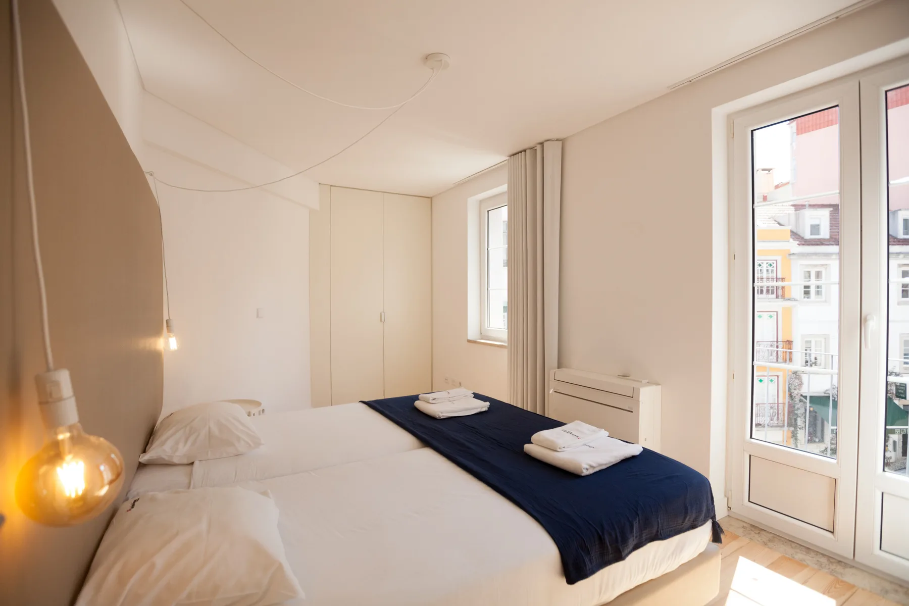 Un dormitorio luminoso con una cama vestida con ropa de cama blanca y azul marino junto a ventanas altas.