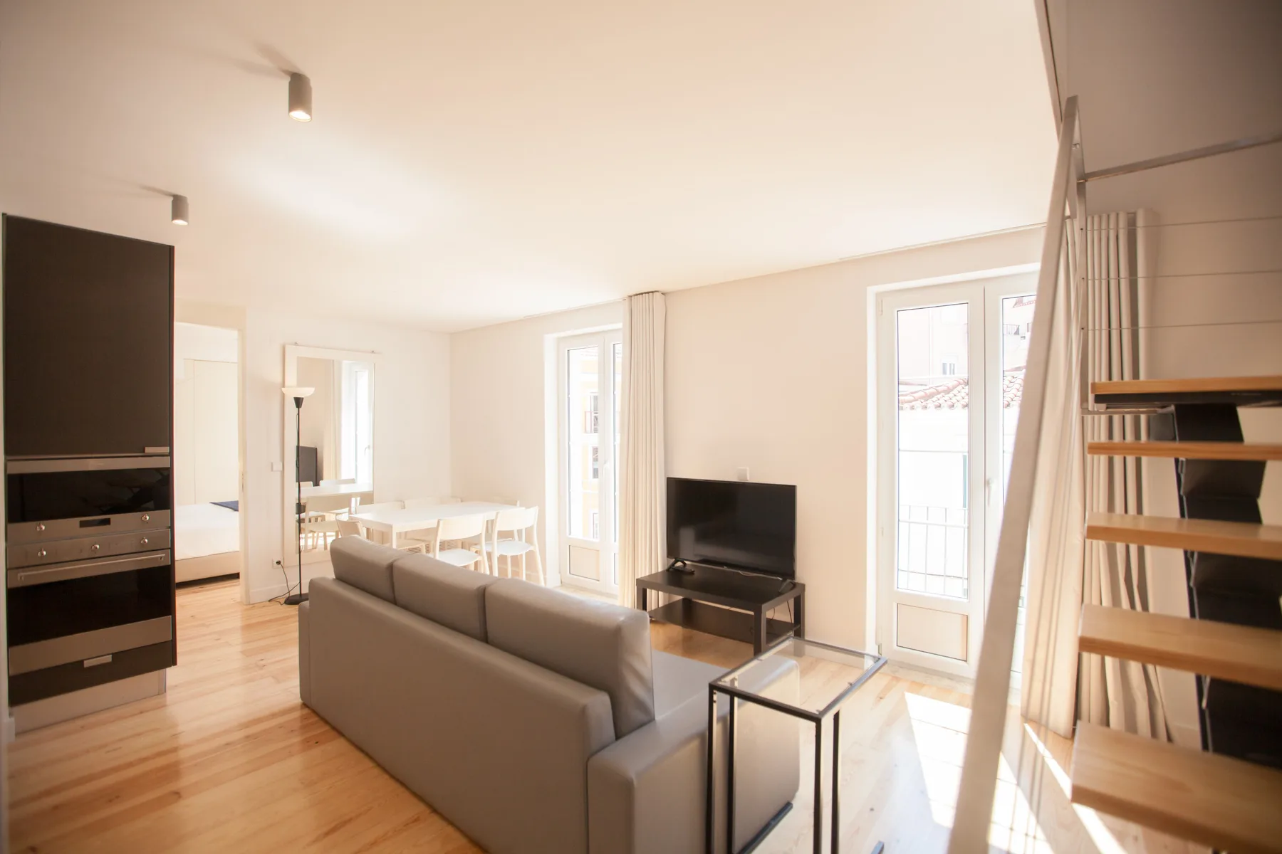 Una sala luminosa con asientos, un televisor y ventanas grandes.