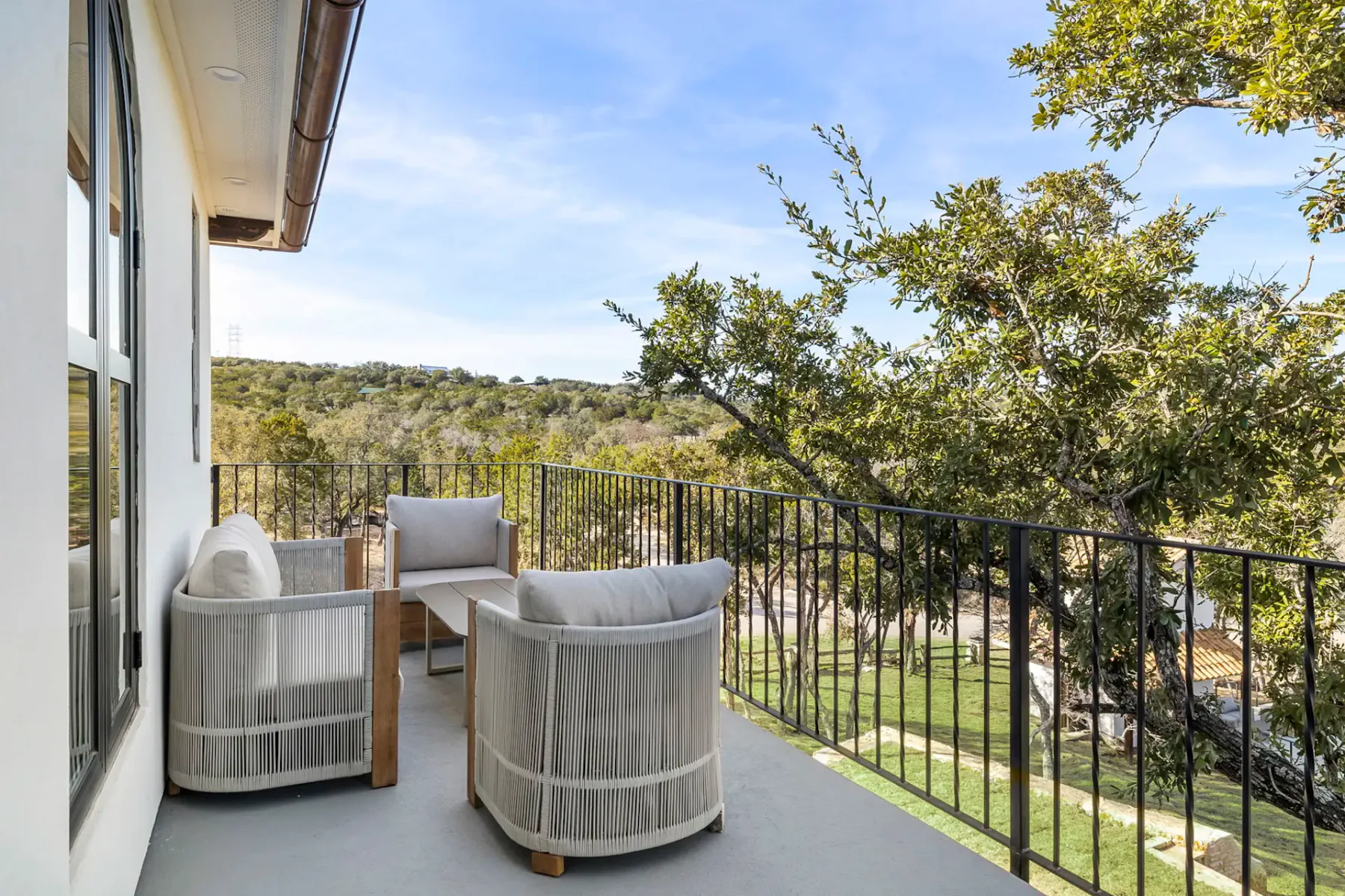 An outdoor balcony with cushioned seating and a view of trees and greenery.